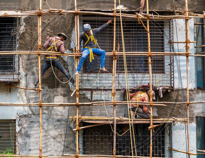 Construction Workers Building A Bamboo Structure On A Building Wall To Initiate The Building Maintenance. No Protective Gears.