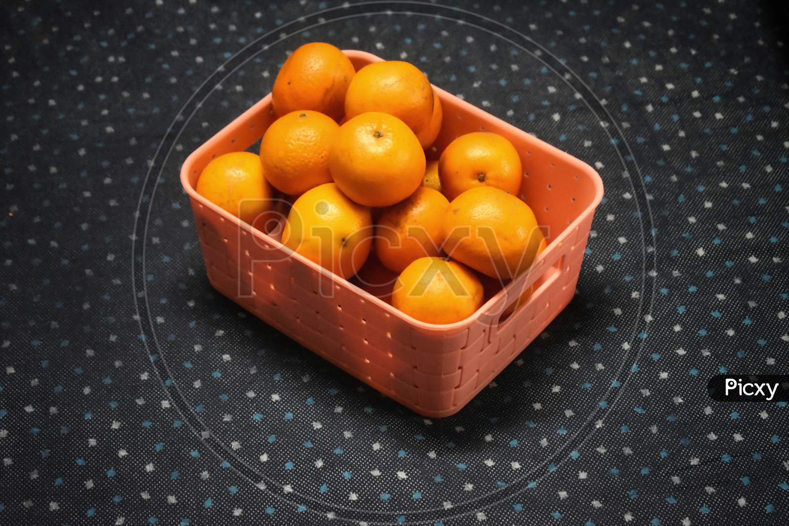A Wicker Basket Full Of Fresh Orange Fruits, Isolated On A Blue And White Dotted Background.