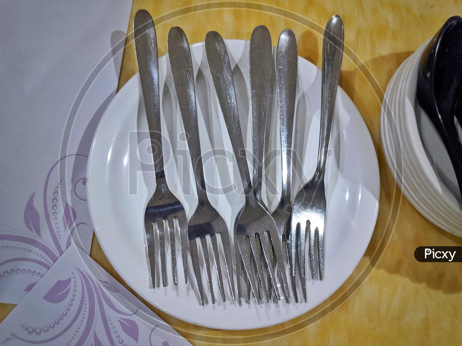 Couple Of Steel Forks On White Plate In Yellow Background