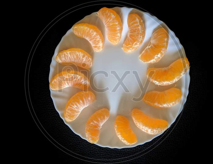 Freshly Cut Natural Healthy Juicy Organic Orange Slices Or Segments On A White Plate, Against A Black Wooden Table, Flat Lay Composition With No People,