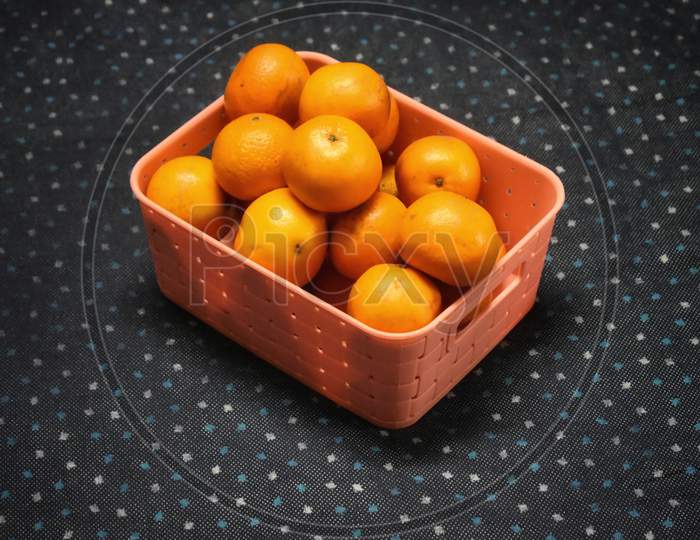 A Wicker Basket Full Of Fresh Orange Fruits, Isolated On A Blue And White Dotted Background.
