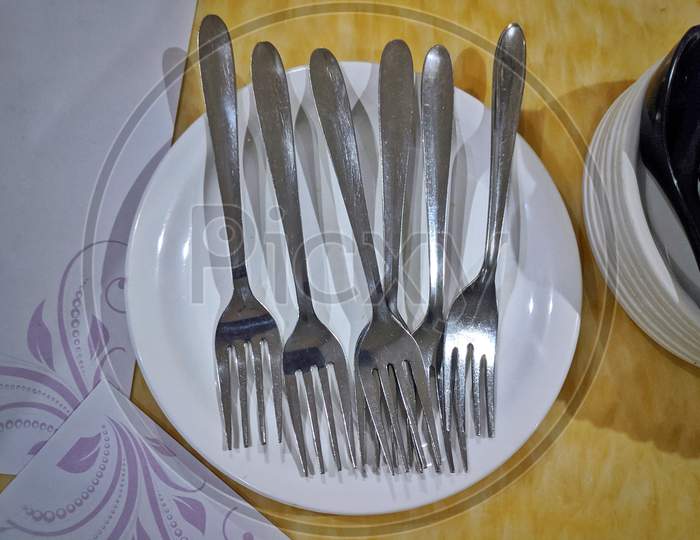 Couple Of Steel Forks On White Plate In Yellow Background