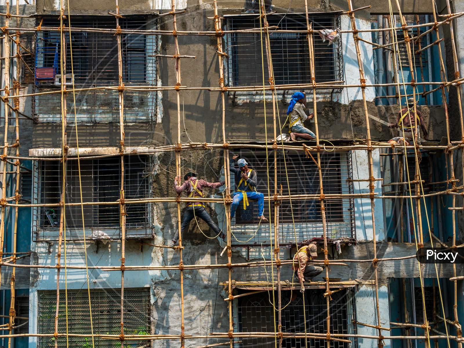Construction Workers Building A Bamboo Structure On A Building Wall To Initiate The Building Maintenance. No Protective Gears.
