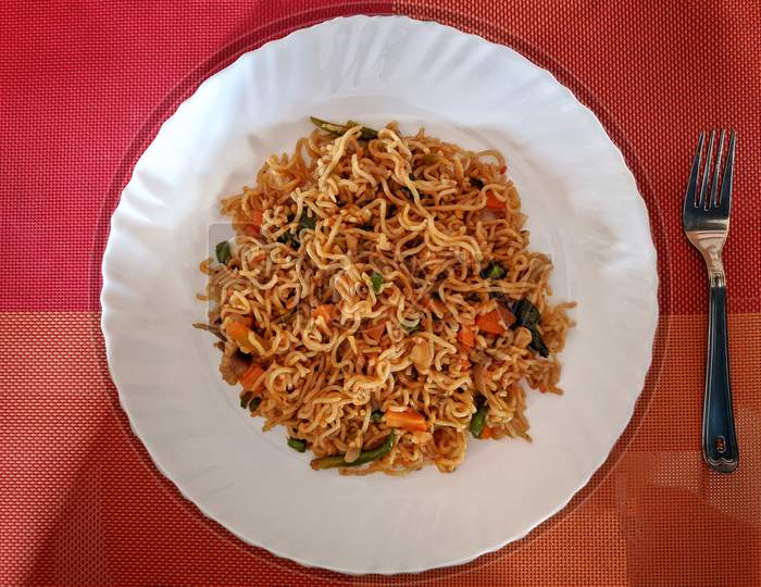 Vegetable Maggi Recipe | Tasty Veg Maggi | Veg Maggi Masala Noodles | Easy Quick Veg Noodles In A White Plate Beside The Forks And Spoon With Colourfull Background, India