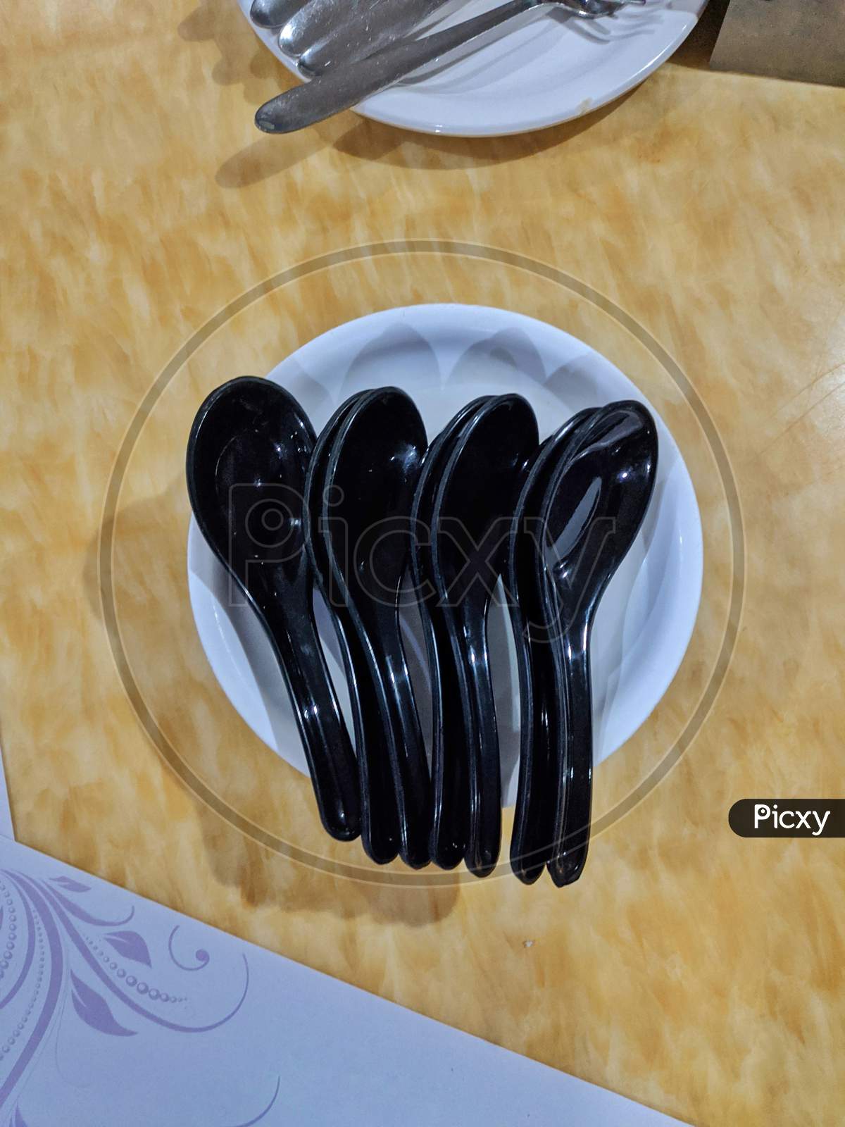 Couple Of Black Spoons On White Plate In Yellow Background