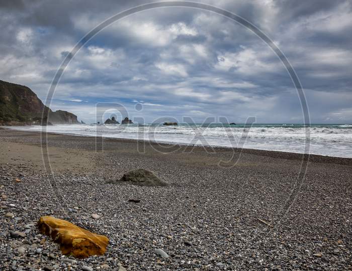 Stormy Weather Approaching An Orange Rock On A Beach In New Zealand