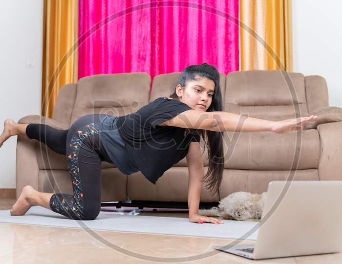 Young Girl Exercising On Yoga Mat By Looking Online Tutorials From Laptop At Home - Concept Of Fitness, Home Gym And Workout Due To Coronavirus Covid-19 Pandemic.