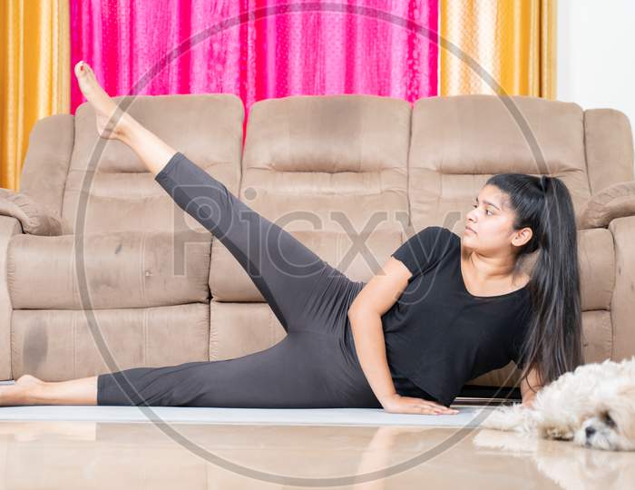 Young Girl With Her Pet Aside Doing Exercise On Yoga Mat At Home - Concept Of New Normal Healthy Lifetyle Due To Coronavirus Covid-19 Pandemic.
