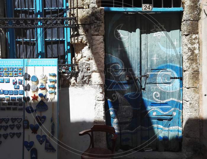 Crete, Greece - October 08, 2017: Front View Of A Colorful Blue Door Next To Shop On A Commercial Street Market With Souvenirs For Tourists With Fridge Magnets On Display