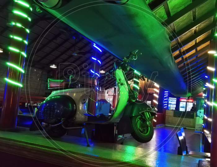 Vintage Retro Two Wheeler Motor Scooter Parked Indoors Against Colorful Lights In An Anonymous Indian Restaurant
