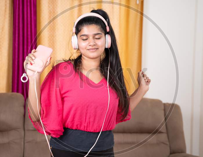 Medium Shot Of Young Girl Dancing By Listening Music From Headphones Connected To Mobile After Workout At Living Room - Concept Of Relaxation, Joyful And Active Healthy Lifestyle
