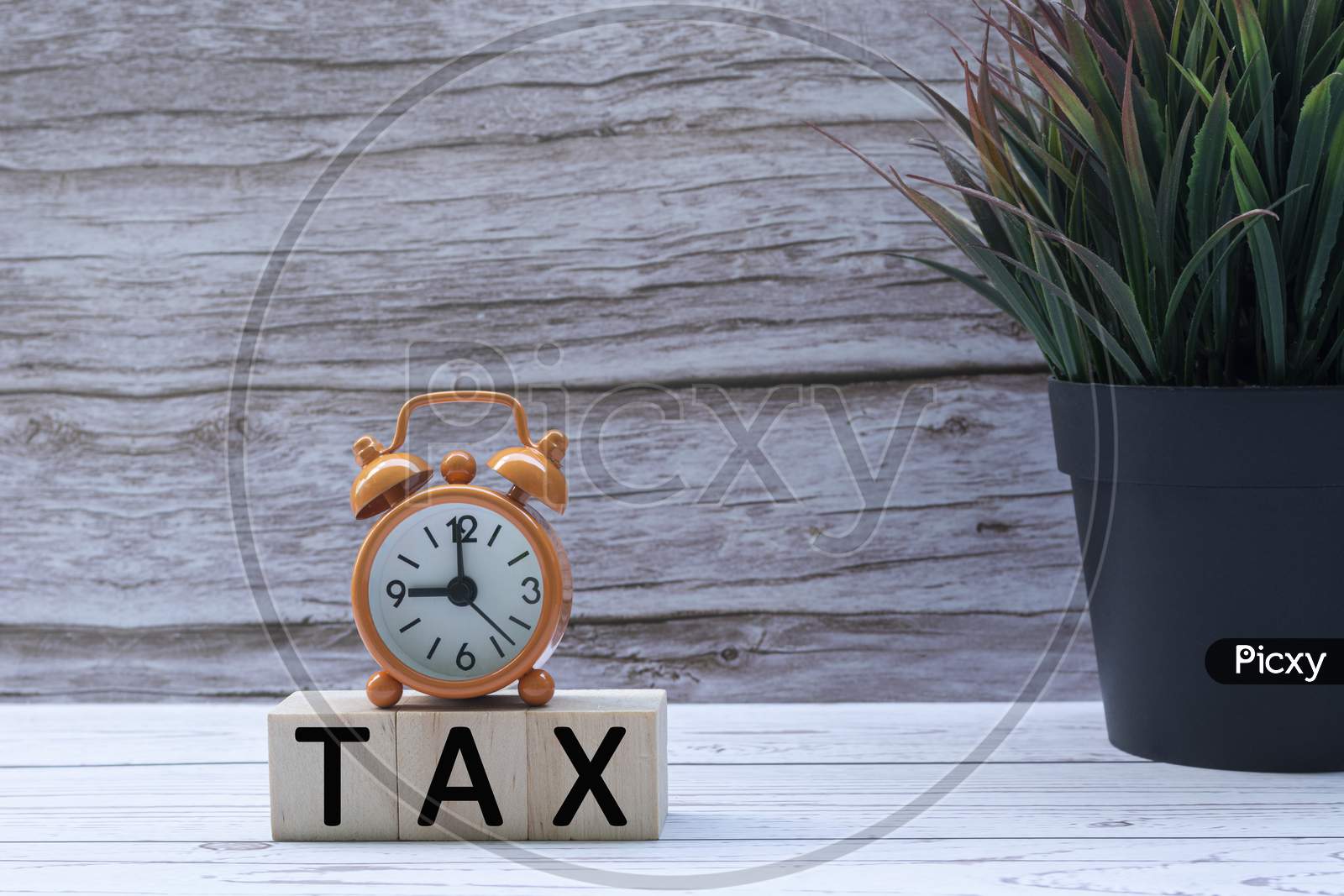 Tax Text On Wooden Block Cube With Alarm Clock And Potted Plant