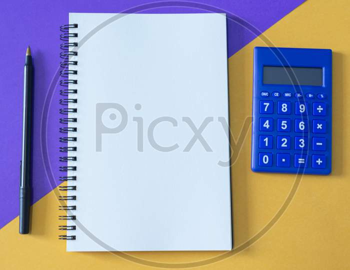 Top View Of Note Pad, Pen, And Calculator On Multi Colored Background