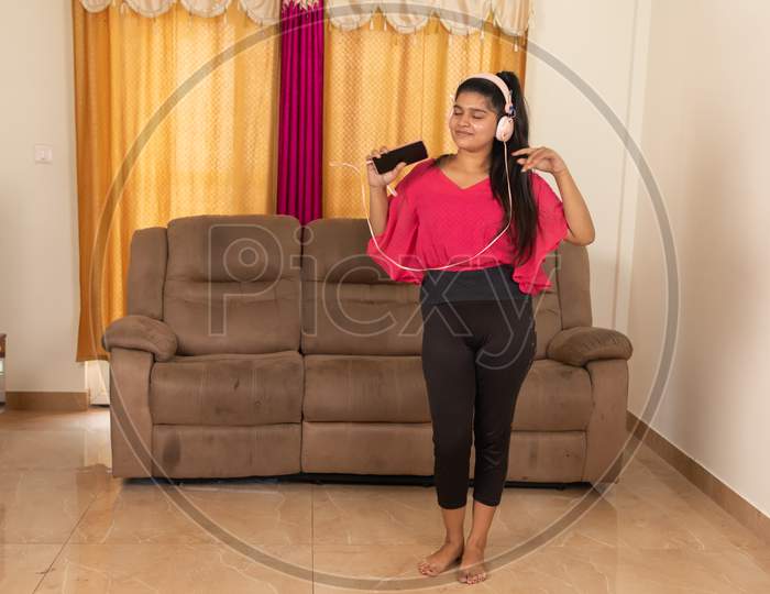 Wide Angle Shot Of Young Girl Dancing By Listening Music On Mobile Using Headphones After Workout At Home - Concept Of Joyful Relaxation And Healthy Lifestyle At Home During Coronavirus Or Covid-19.