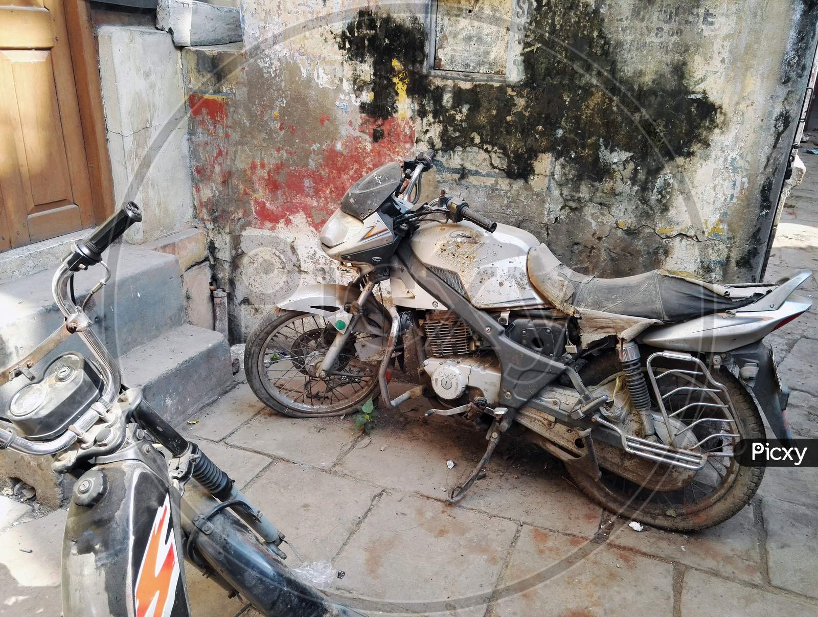 Varanasi, India - November 01, 2016: An Old Rusty Damaged And Flat Tired Indian Motor Bike Parked In A Grungy Corner Of An Alley In The Old City, Uttar Pradesh