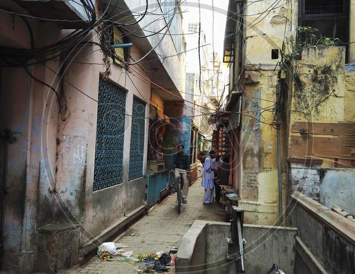 Varanasi, India - November 01, 2016: Narrow Gali Or Lane Or Street Between Old Buildings With Messy Electrical Wire And A Man Riding Bicycle. Uttar Pradesh.