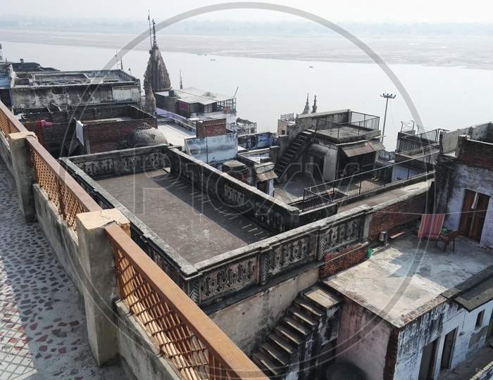 Varanasi, India - November 01, 2016: Ancient City Connected Rooftop View With Old Buildings Near Ganges River And Grunge Historical Roofs. Houses Terrace With Stairs Against Foggy River. Uttar Pradesh