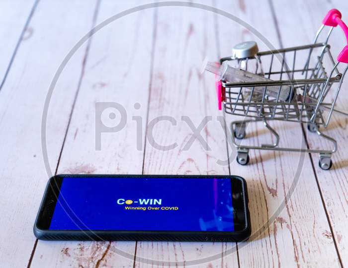 Mobile Phone With Co-Win App Logo On The Screen With A Small Shopping Cart With A Syringe And Vial Showing The Shopping And Tracking Of Covaxin Covishield Purchase From Hospital Or Pharmacy To Increase Immunity