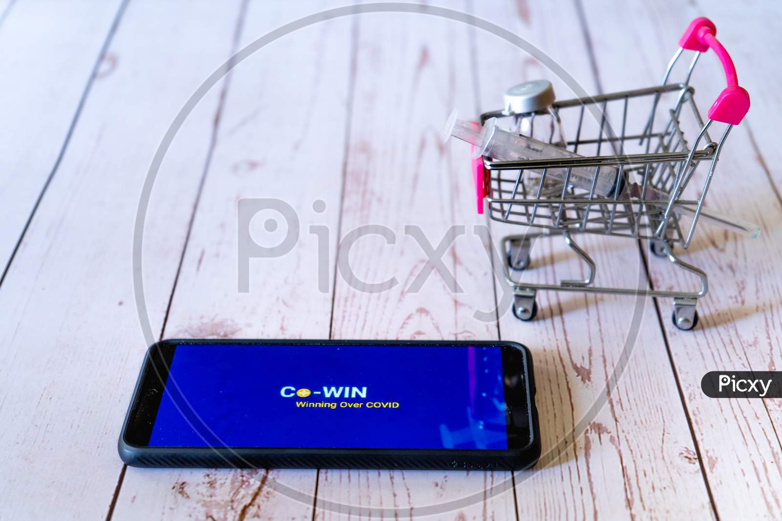 Mobile Phone With Co-Win App Logo On The Screen With A Small Shopping Cart With A Syringe And Vial Showing The Shopping And Tracking Of Covaxin Covishield Purchase From Hospital Or Pharmacy To Increase Immunity