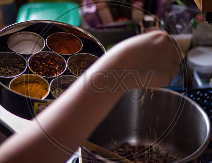 A Lady Preparing Indian Spicy Food. Home Cooking Concept With Various Spices Such As Red Chill, Salt And Turmeric Being Chosen Picked And Carefully Sprinkled In A Cooker With Vegetable