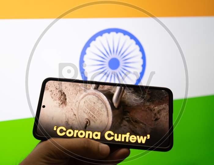 Man Holding A Mobile Phone With News On Corona Curfew And The India Tri Color Flag In The Background Showing The Self Lockdown During The Second Stage Of The Pandemic