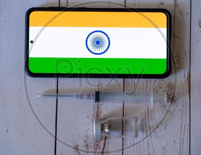 Mobile Phone With App Showing Indian Flag With A Syringe And Small Glass Bottle Vial Of Medicine Placed On The Side Showing Vaccination For Covid19 Chicken Pox, Polio, Tubercolosis, Rabies And More In Delhi India Being Tracked Online