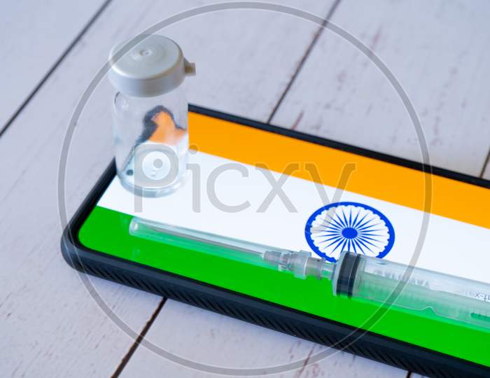 Mobile Phone With App Showing Indian Flag With A Syringe And Small Glass Bottle Vial Of Medicine Placed On The Side Showing Vaccination For Covid19 Chicken Pox, Polio, Tubercolosis, Rabies And More In Delhi India Being Tracked Online