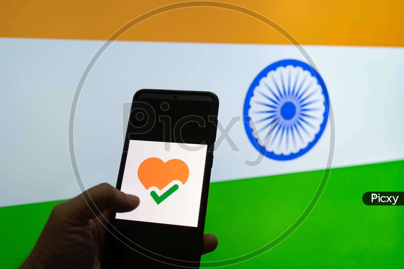 Man Holding Mobile Phone With The Arogya Setu App In Front Of A Flag Of India Showing How Technology Is Helping Contact Tracing In Covid 19 Pandemic