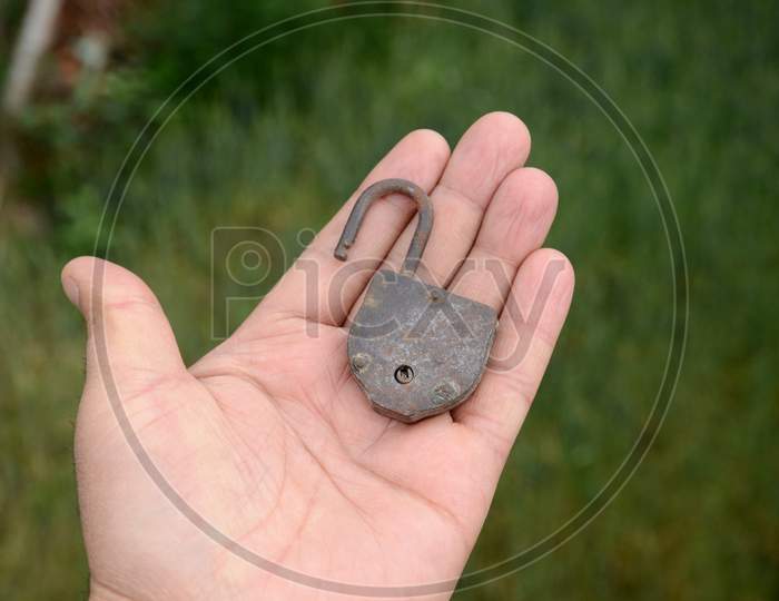 The Old Dark Metal Iron Door Lock Hold On Hand Over Out Of Focus Green Background.
