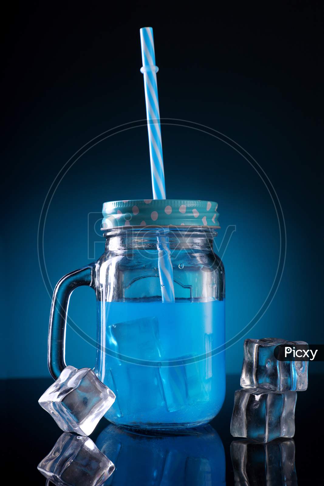 Blue Colored Cocktail In A Mason Jar With Straw And Ice Cubes