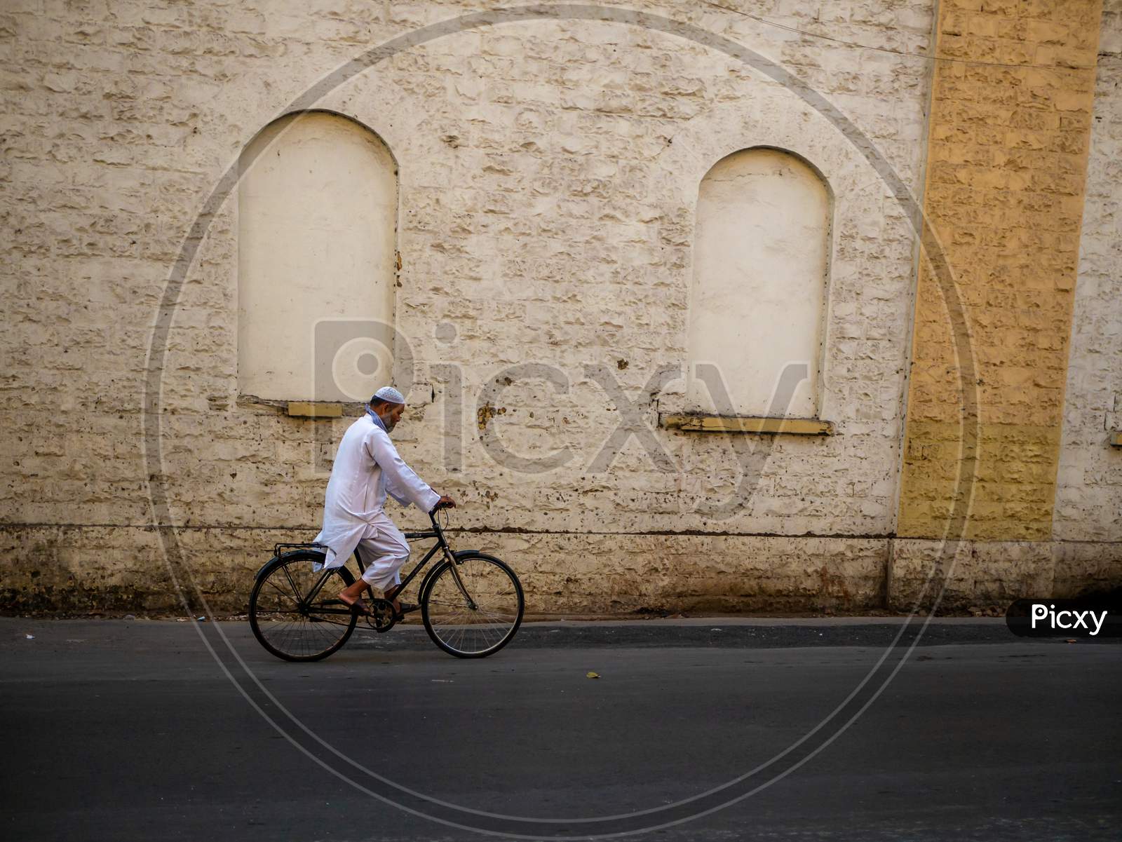 Muslim Old Age Man Wearing Traditional Islamic Clothes And Skull Cap Riding A Bicycle On The Streets Of Mumbai