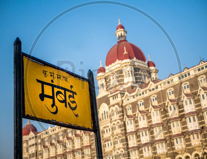 Mumbai Signboard In Marathi Language With Heritage Grand Class Five-Star Hotel Taj, Next To The Gateway Of India.