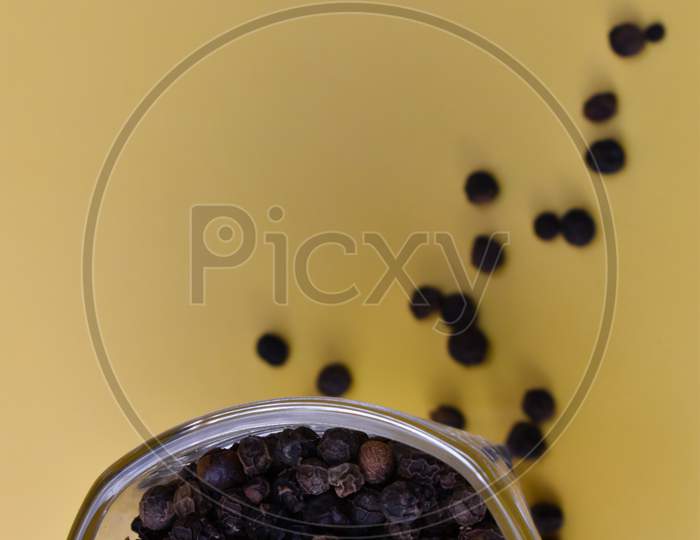 Selective focus closeup of a dried black pepper seed in a glass bowl