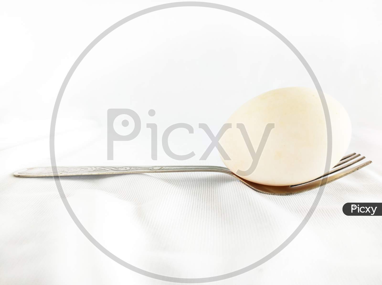An Egg Picked Up In A Fork On Top Of A White Cloth