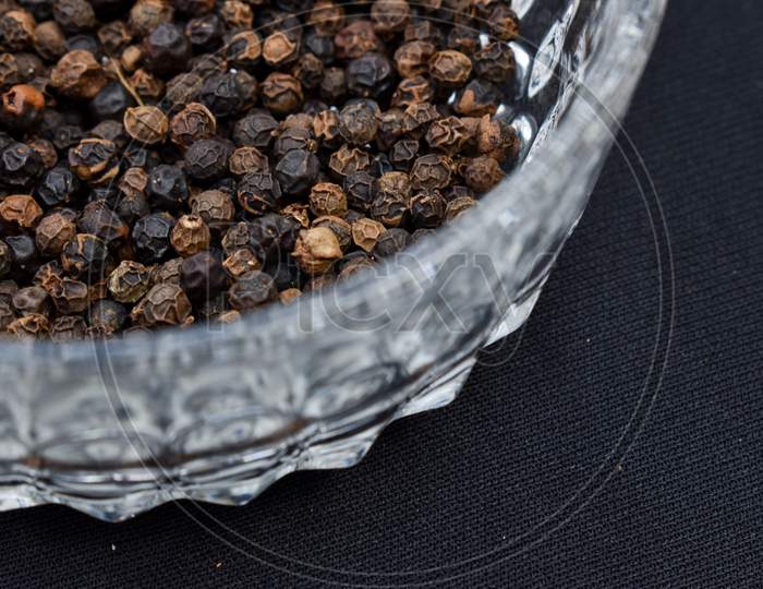 Selective focus closeup of a dried black pepper seed in a glass bowl