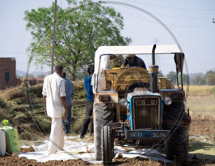 Wide Shot Of Tractor With Seperator Fan Being Used To Seperate Grain From Husk With Farmers Putting Grain Into The Tractor And The Husk Being Blown Out Of The Side