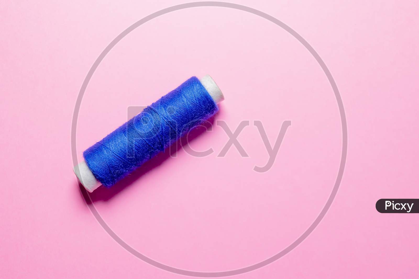 Sewing Machine Thread Reel Of Blue Color On Pink Background With Selective Focus.