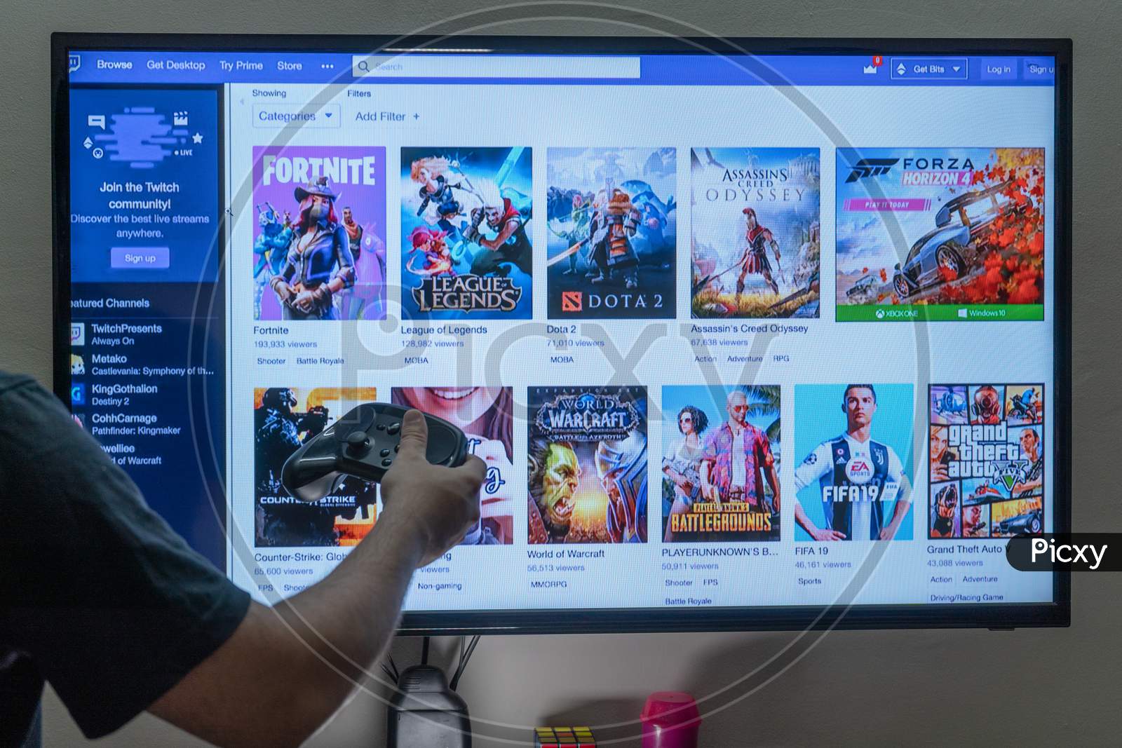 Man Holding A Steam Remote In Front Of A Pc Console Screen Showing Twitch Streaming Platform Base Screen With Games Where People Are Streaming Fulltime To Earn Money