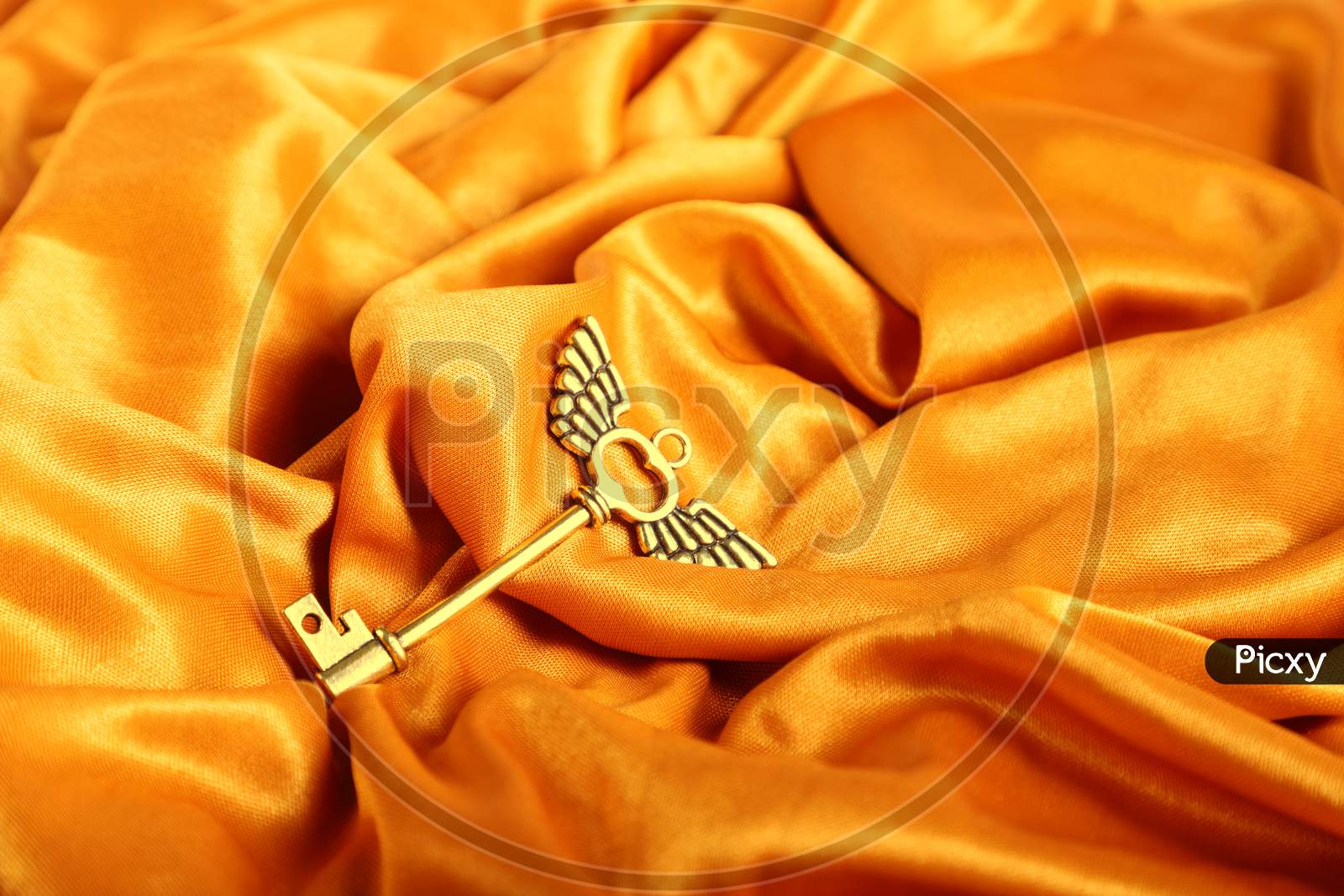 Golden Antique Key With Wings On A Golden Satin Background