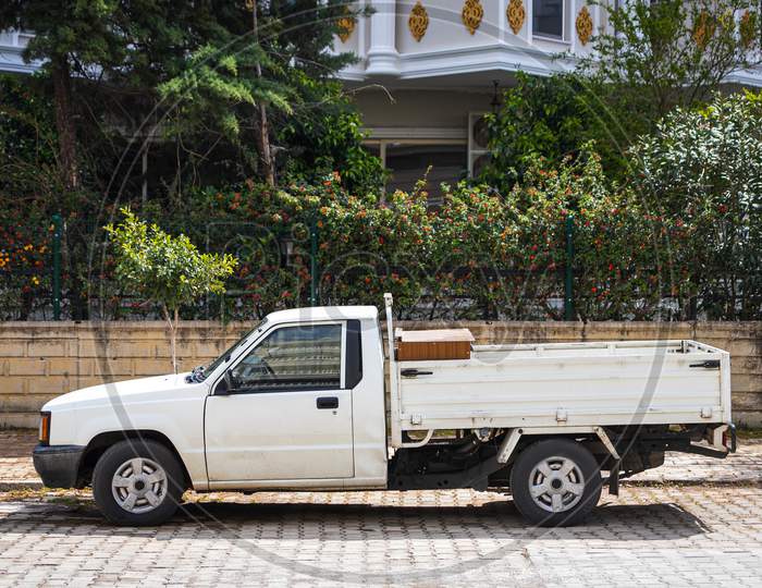 White Pickup  Is Parked  On The Street On A Warm Summer Day Against The Backdrop Of A Parking