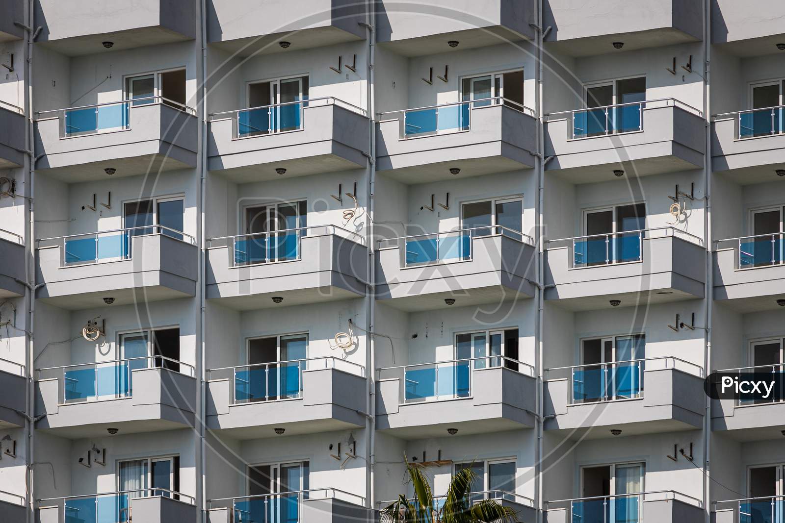 A White Residential Building With Flat, Identical Balconies With Ripped Air Conditioners And Broken Glass. Balcony Pattern