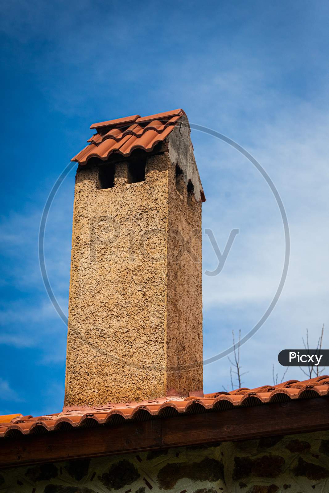 Stone Tall Chimney With Tiles On The Roof Of A Country House Against The Blue Sky