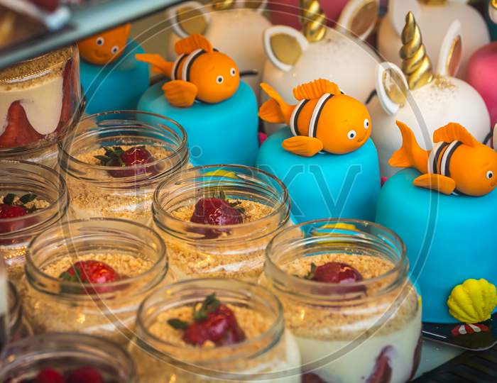 Close-Up Of Creamy Mousse Cake In Small Jars Decorated With Strawberries And Cake For Children With Fish And Unicorns
