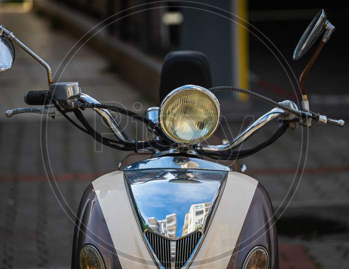 A Vintage  White   Motorcycle, Moped  Stands In A Parking Against The Backdrop Of  Gray Wall. Front  View