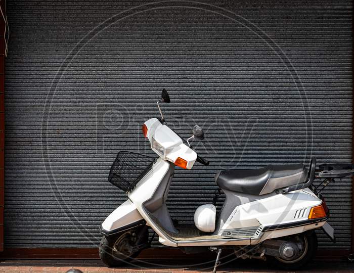A Vintage  White   Motorcycle, Moped  Stands In A Parking Against The Backdrop Of  Gray Wall. Side View