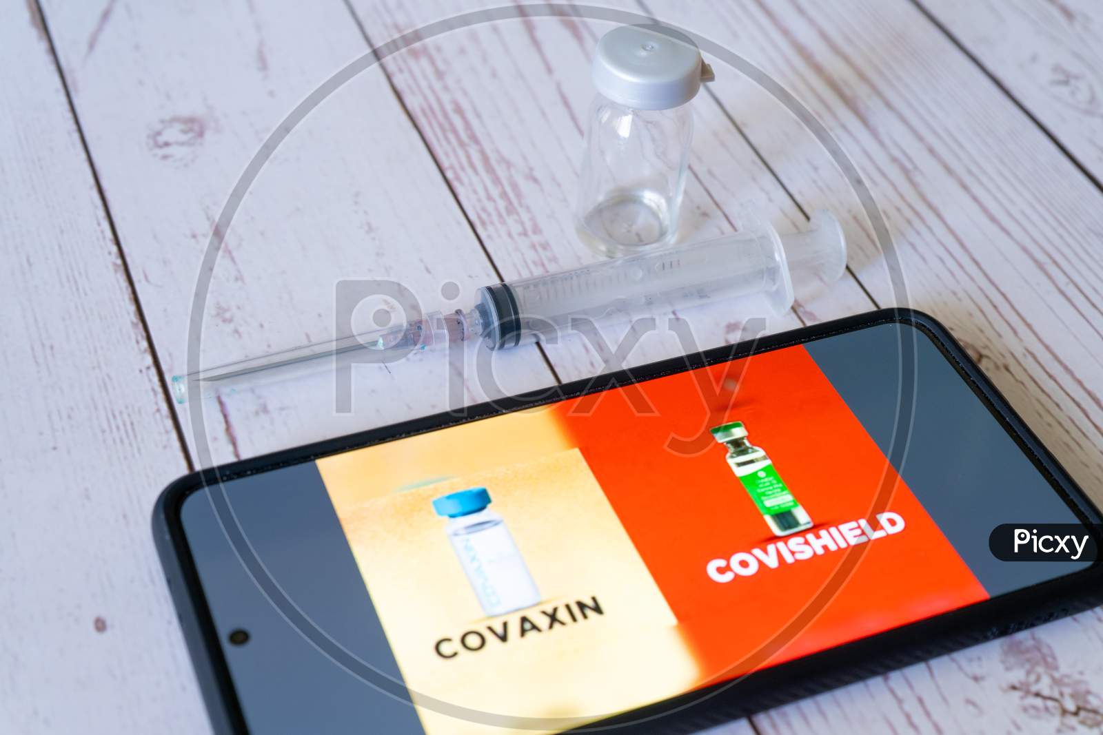 Mobile Phone Showing The Covid 19 Coronavirus Vaccines Covishield Covaxin For Selection In The Co-Win App With Syringe And Vial On The Side