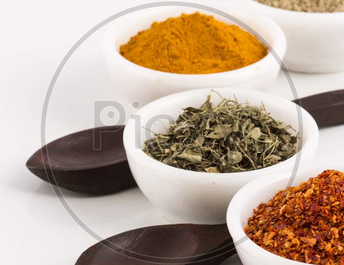 Various Spices In Ceramic Bowls With Wooden Spoons Isolated On White Background. Stock Photo