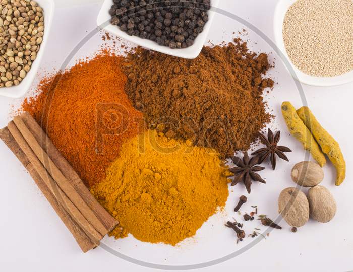 Spices: Turmeric, Chilly Powder, Black Pappercorns In Ceramic Bowls And Cinnamon, Anise Stars On Ground With White Background Stock Photo