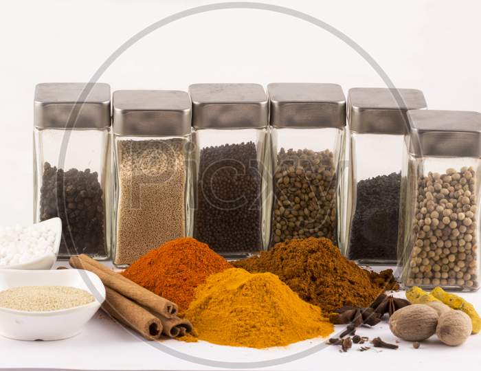 Spices: Turmeric, Chilly Powder, Nutmegs And, Anise Stars With Glass Bottles On Ground With White Background Stock Photo