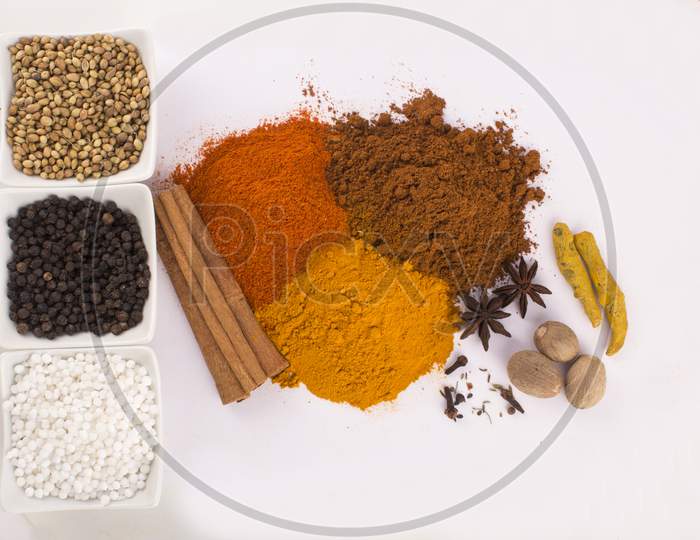 Spices: Turmeric, Chilly Powder, Black Pappercorns In Ceramic Bowls And Cinnamon, Anise Stars On Ground With White Background Stock Photo